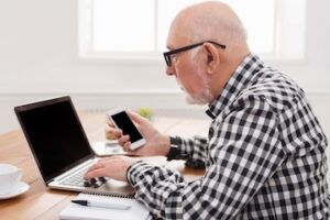 elderly man works on laptop and smartphone